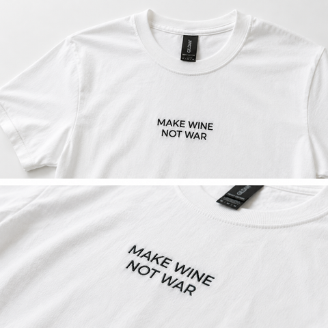 White short-sleeve crewneck T-shirt with the slogan 'MAKE WINE NOT WAR' printed in black sans-serif text on the chest. The image is a two-panel close-up showing the front graphic and the inner neck label.